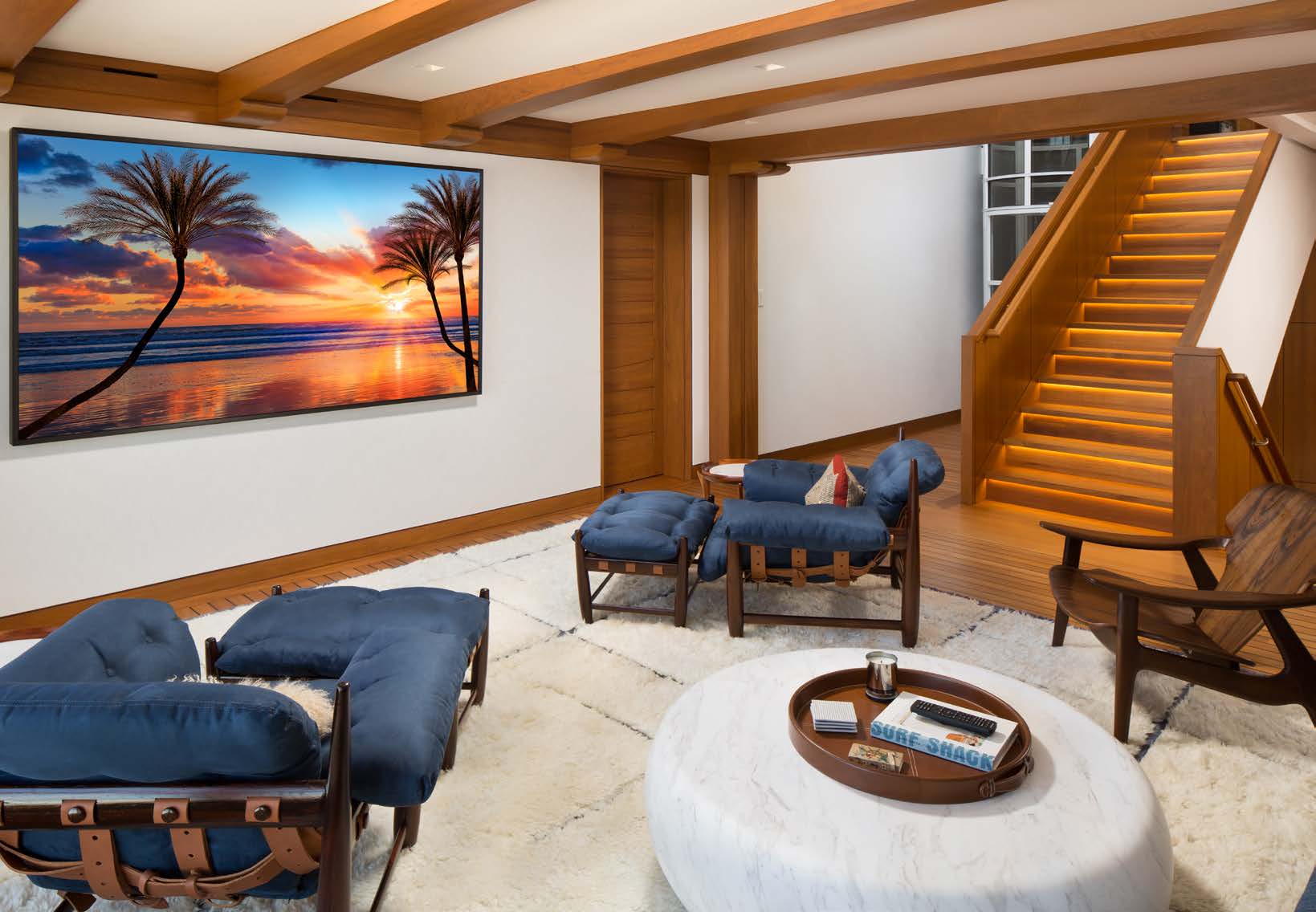 The 98-inch 4K display showing a Pacific sunset scene beside the home's illuminated staircase.