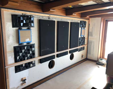 Construction view — speakers, subwoofer openings, and absorber tiles built into the front wall before the acoustically transparent fabric was installed.